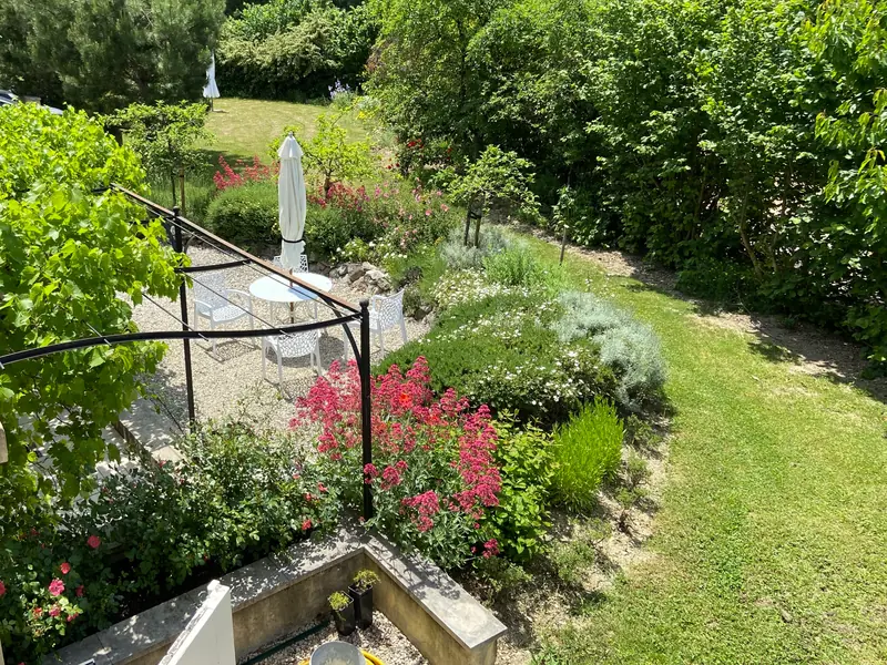 De tuin van de studio van bovenaf: het terras met een witte tafel en stoelen onder de pergola, borders met valeriaan en het grasveld